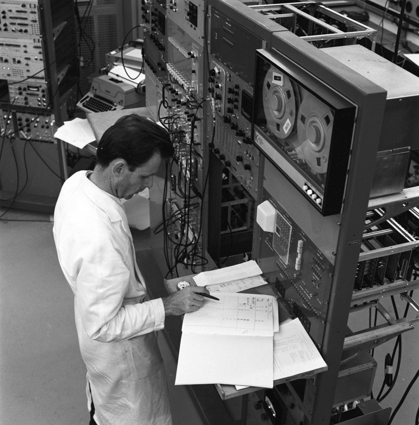 Homme en blouse blanche écrivant dans un carnet de bord entouré de machines
