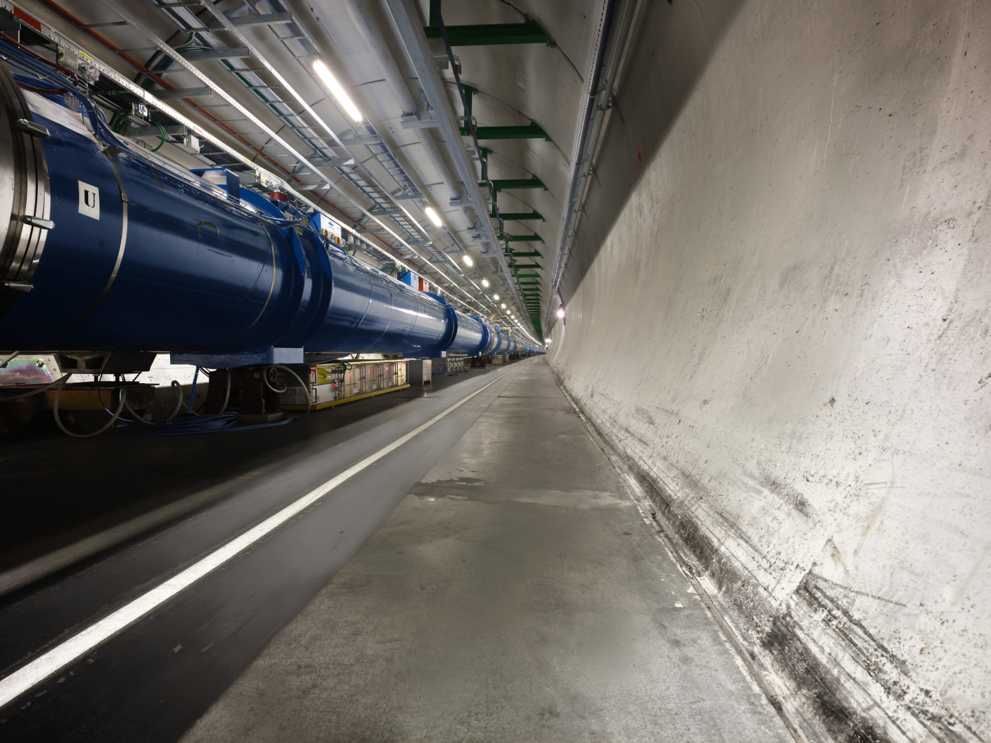 View of the LHC accelerator in the tunnel: a chain of magnets which looks like big blue and silver cylinders.