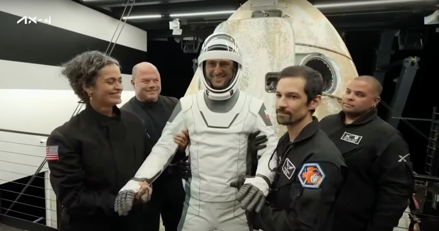 An astronaut emerging from a spacecraft is supported by 4 people