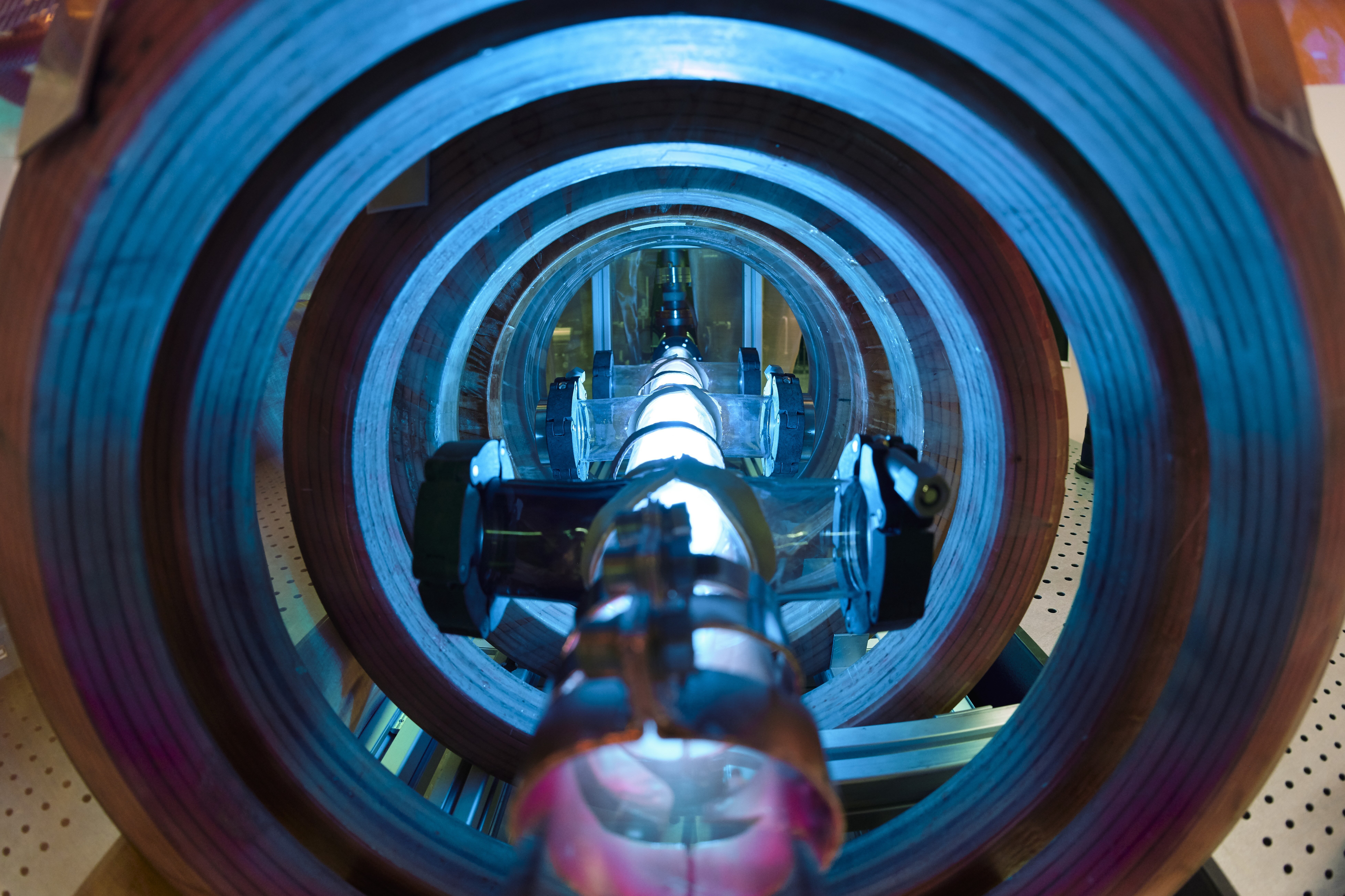 Blue glowing tube, with slight red glow at one end, surrounded by metal rings.