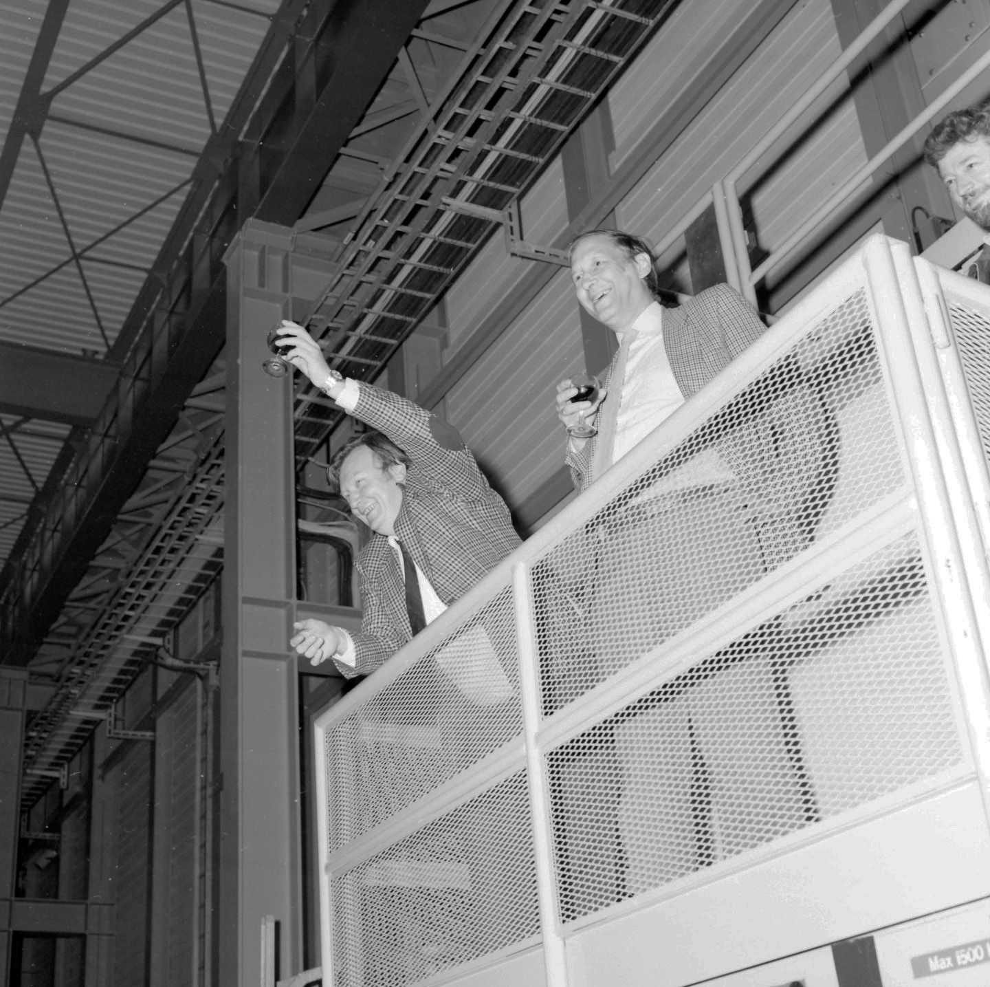 Two men standing on a high platform holding wine glasses