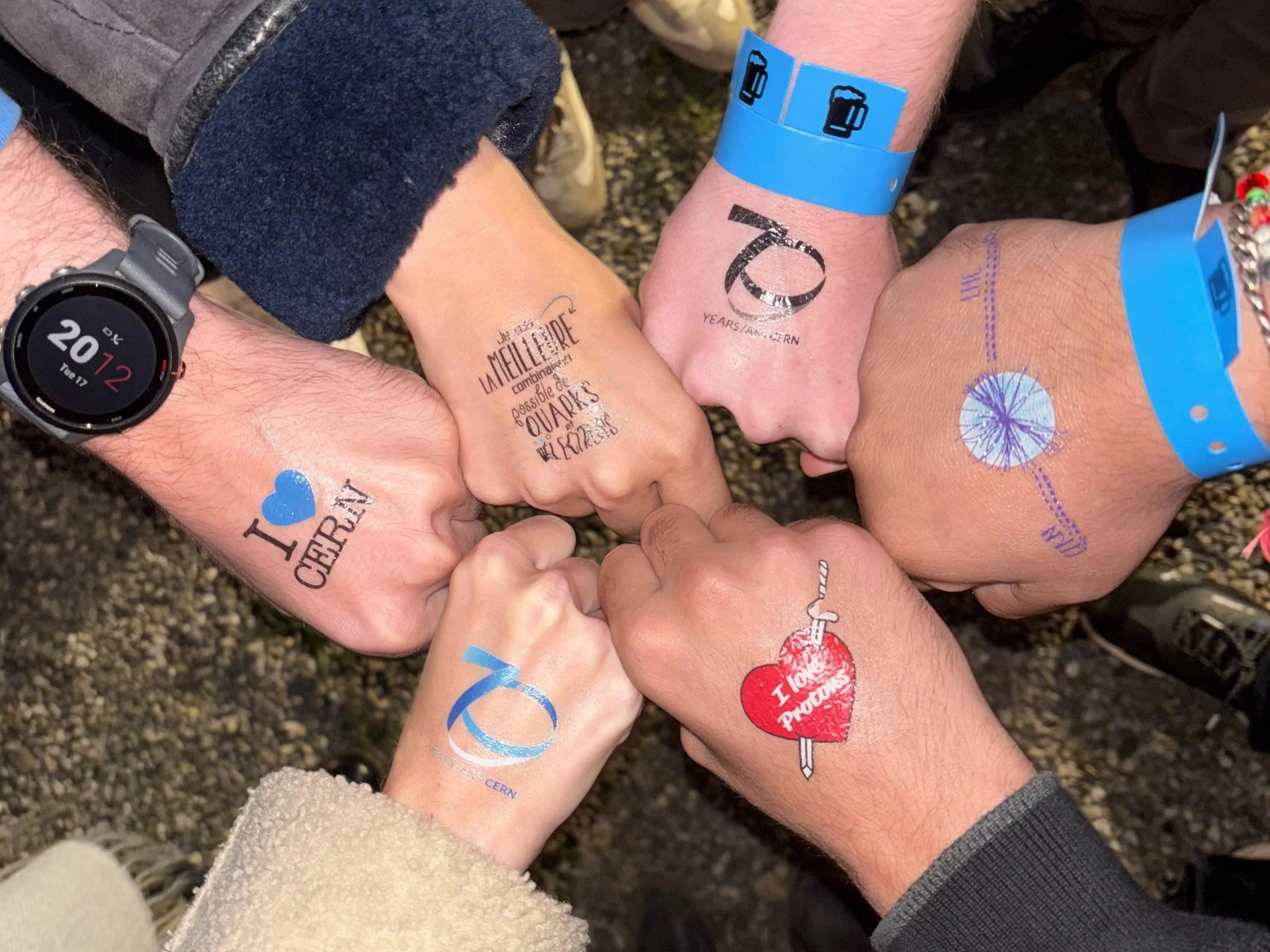 6 hands with tattoos touching in a circle