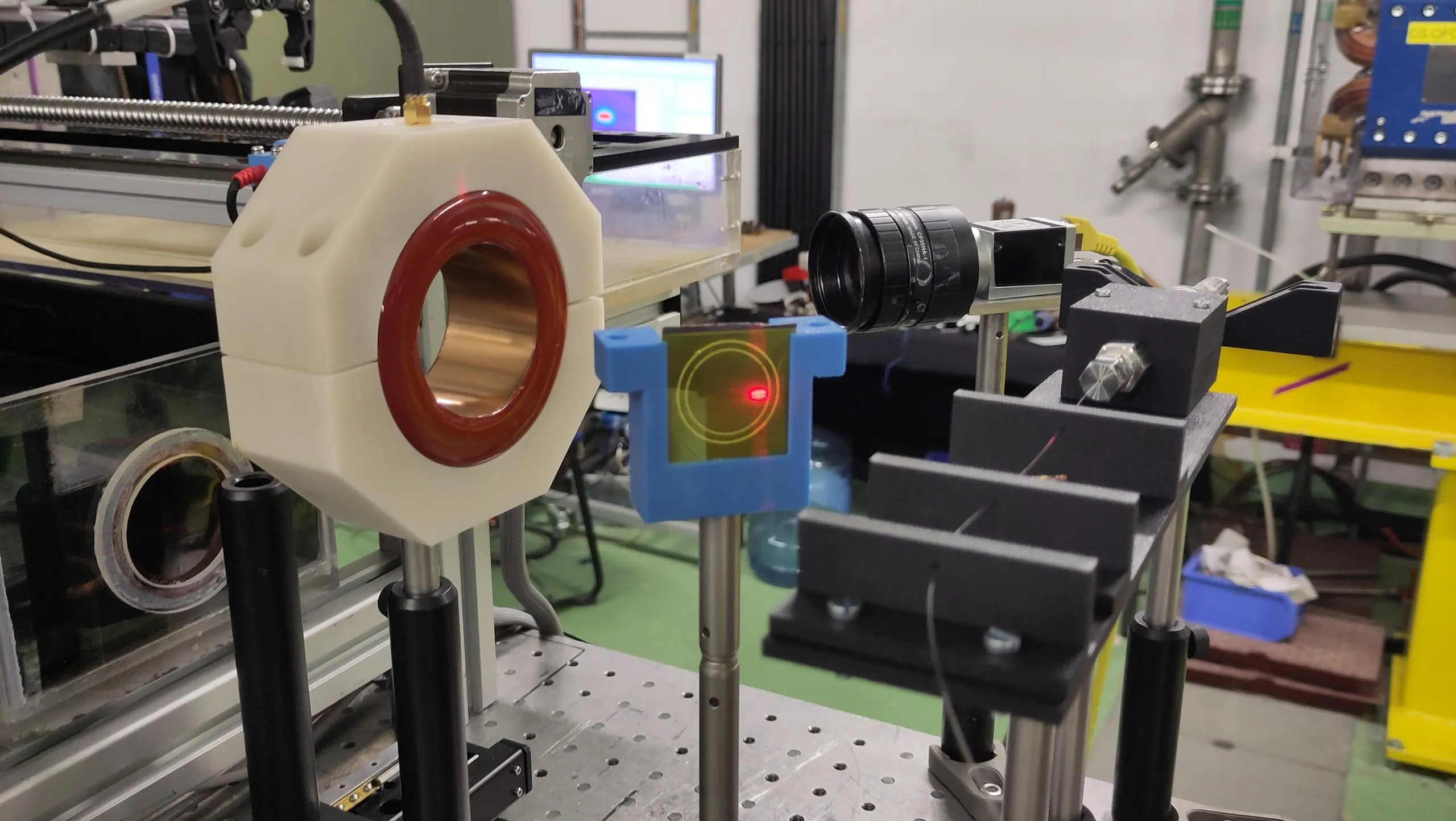 An optic fibre (a thin transparent wire) is positioned between two support next to a small screen on which a red dot is seen
