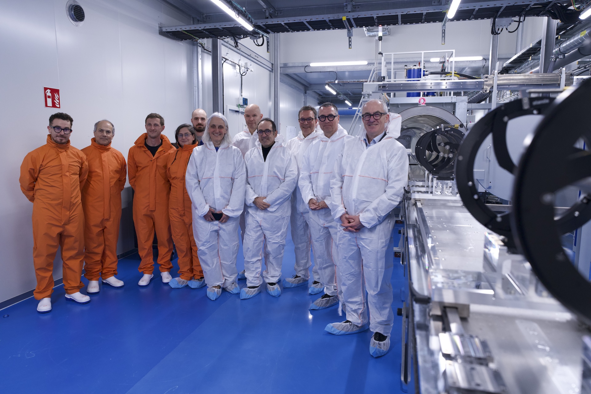CERN Director-General Mark Thomson (furthest right) with members of the Directorate (wearing white clean room suits) and the project team (wearing orange clean room suits), next to the beryllium beam-pipe welding machine. (Image: CERN)