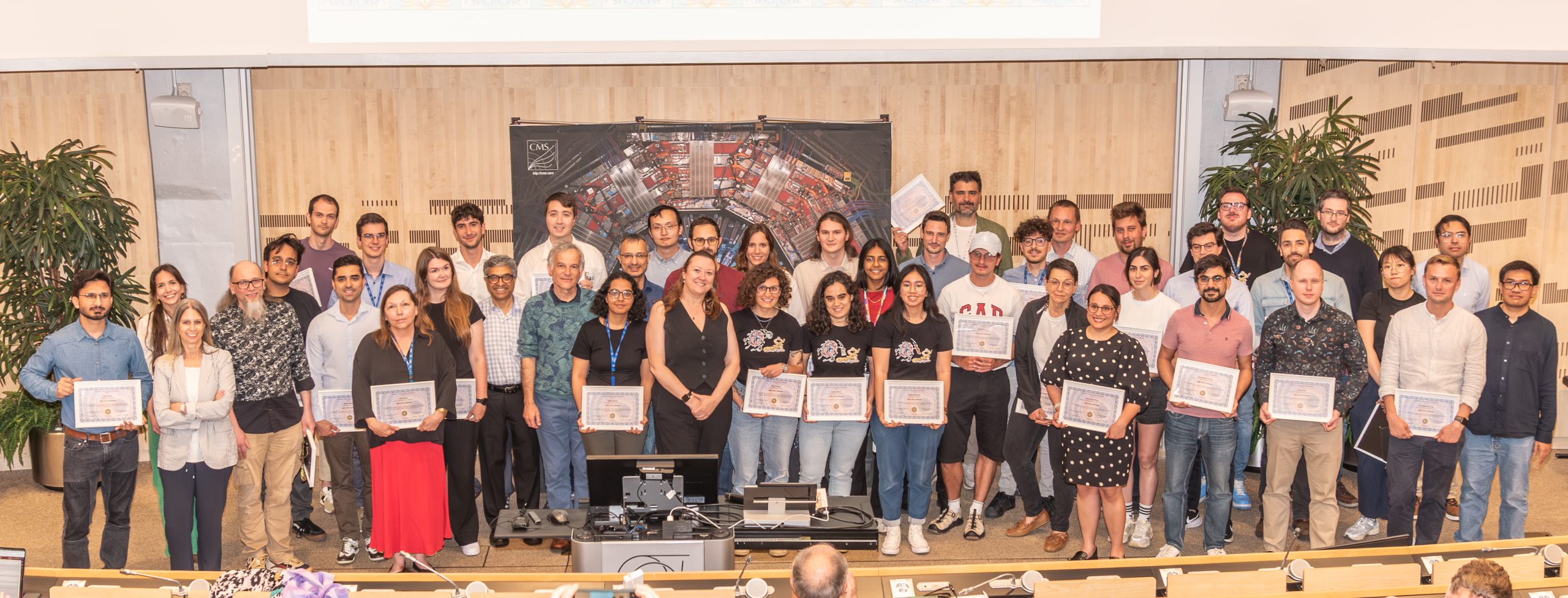A large group standing at the front of the CERN auditorium, most of them carrying framed certificates