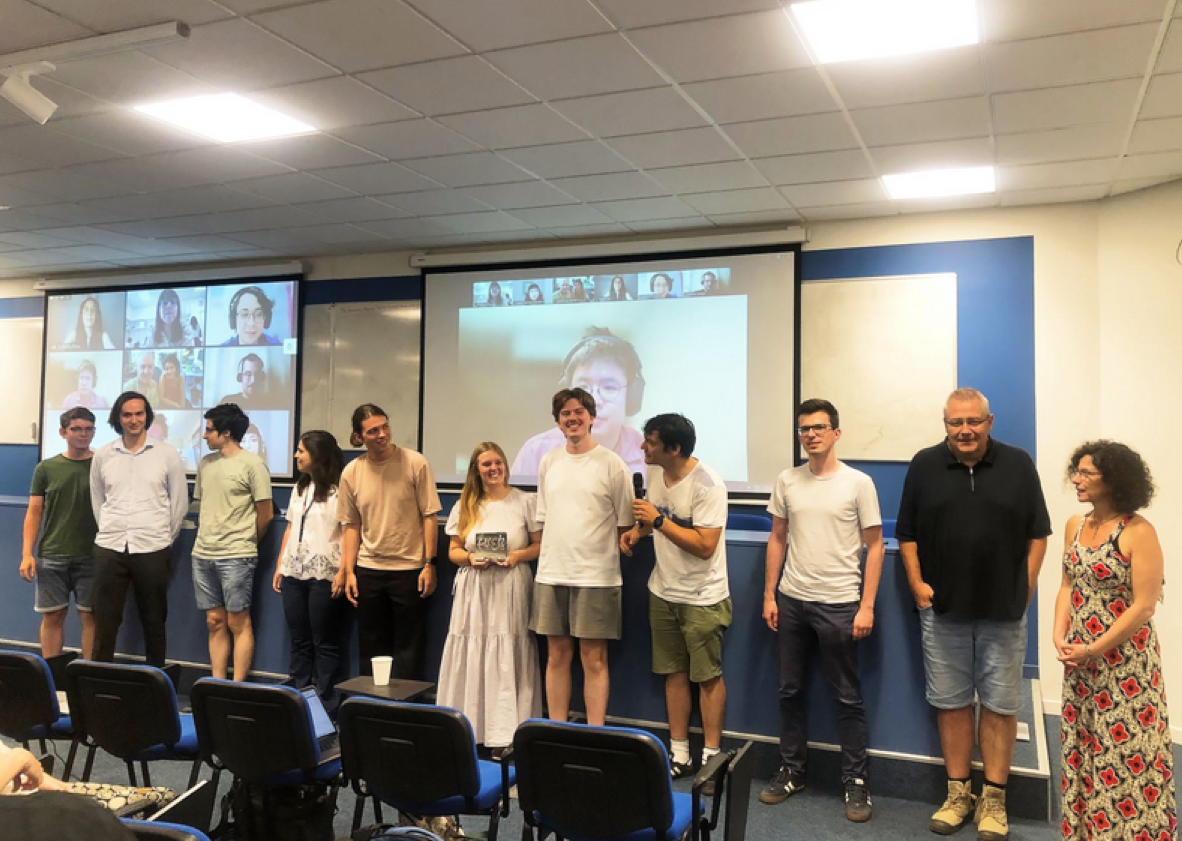 People standing in a line in front of a screen showing people on Zoom