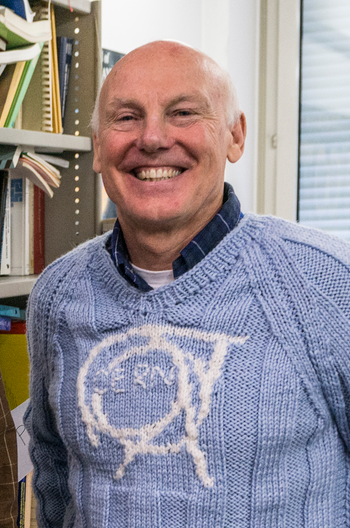 Mick Storr smiling in a light blue knitted jumper with the CERN logo on the front