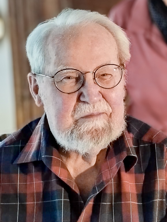 Jens Bisplinghoff with white hair, a white beard, and round black glasses. He is wearing a brown and black checked shirt.