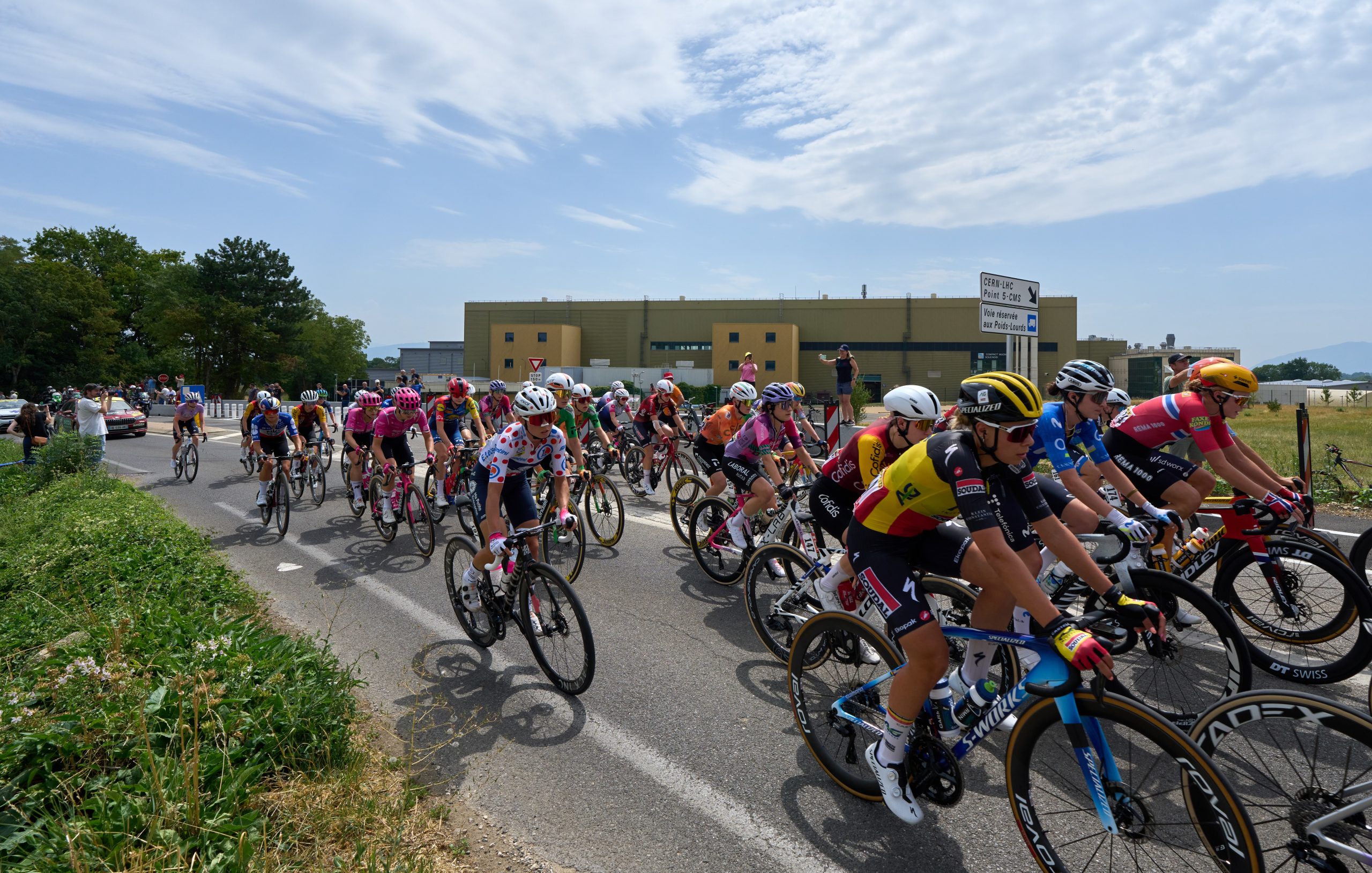 Cyclists cycling past a sign reading 'CERN-LHC Point 5-CMS
