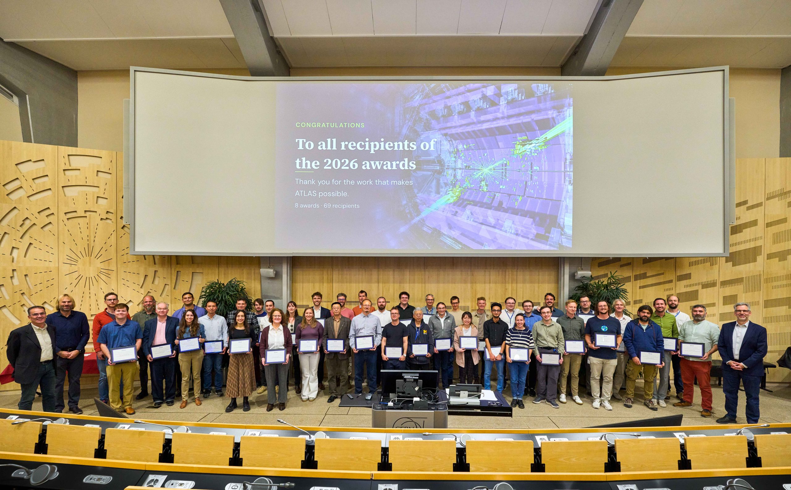 Winners of the ATLAS Outstanding Achievement Awards stood in front of a screen reading "Congratulations to all recipients of the 2026 awards. Thank you for all the work that makes ATLAS possible. 8 awards - 69 recipients